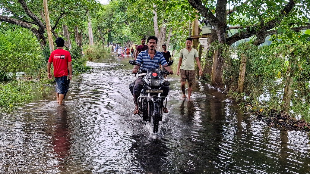 5-West Bengal-Paschim Medinipur--- A man rides a motorcycle as people wade through a waterlogged road following flooding in Dangabari village, in Sabang, Paschim Medinipur district, West Bengal,.jpg